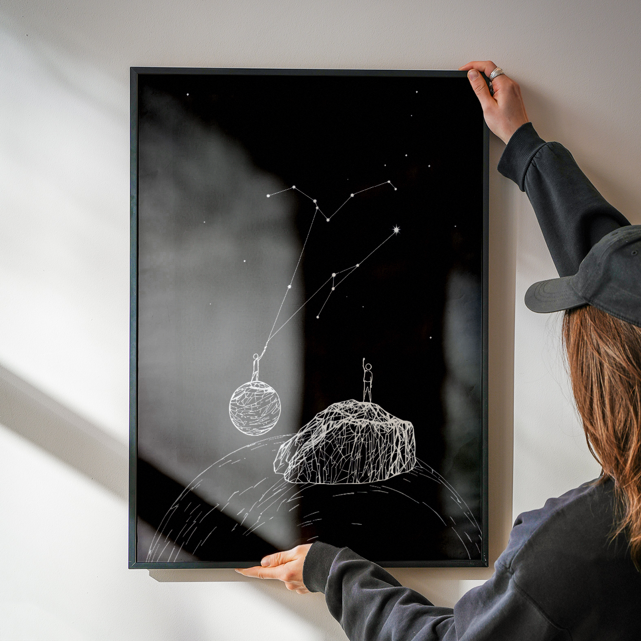 Person hanging a framed black and white artwork on a wall