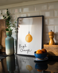 Kitchen counter with a framed print of an orange, a bowl of oranges, and a vase.