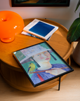 Table with a framed artwork of a woman holding a bird, an orange lamp, and books.