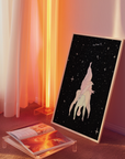 Framed wall art with a starry night sky, placed on the floor with a magazine next to it.