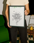 Person holding a framed black and white lotus flower art print in a room with green sofa and wooden table.