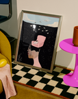 Framed artwork of a woman with a pink chair on a checkered floor.