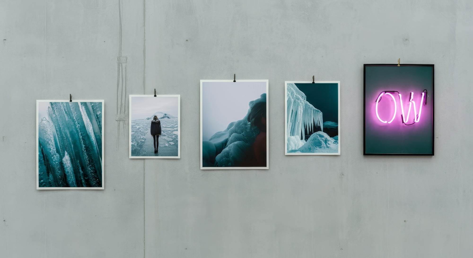 Five framed artworks on a gray wall, including a neon sign.