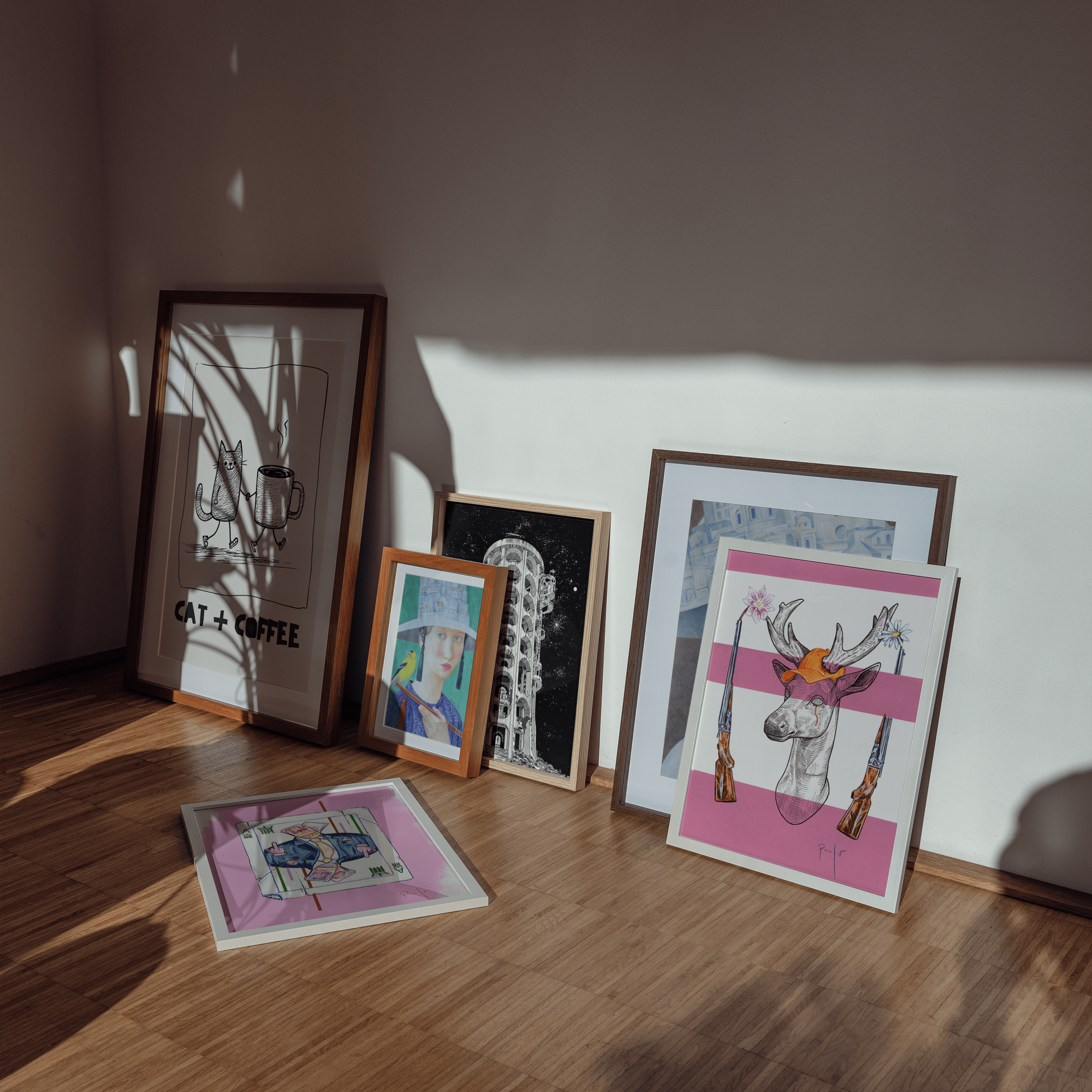 Collection of framed artworks on a wooden floor with a neutral wall background