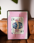 Framed artwork of a person in a card design on a pink background, placed on a brown leather sofa.