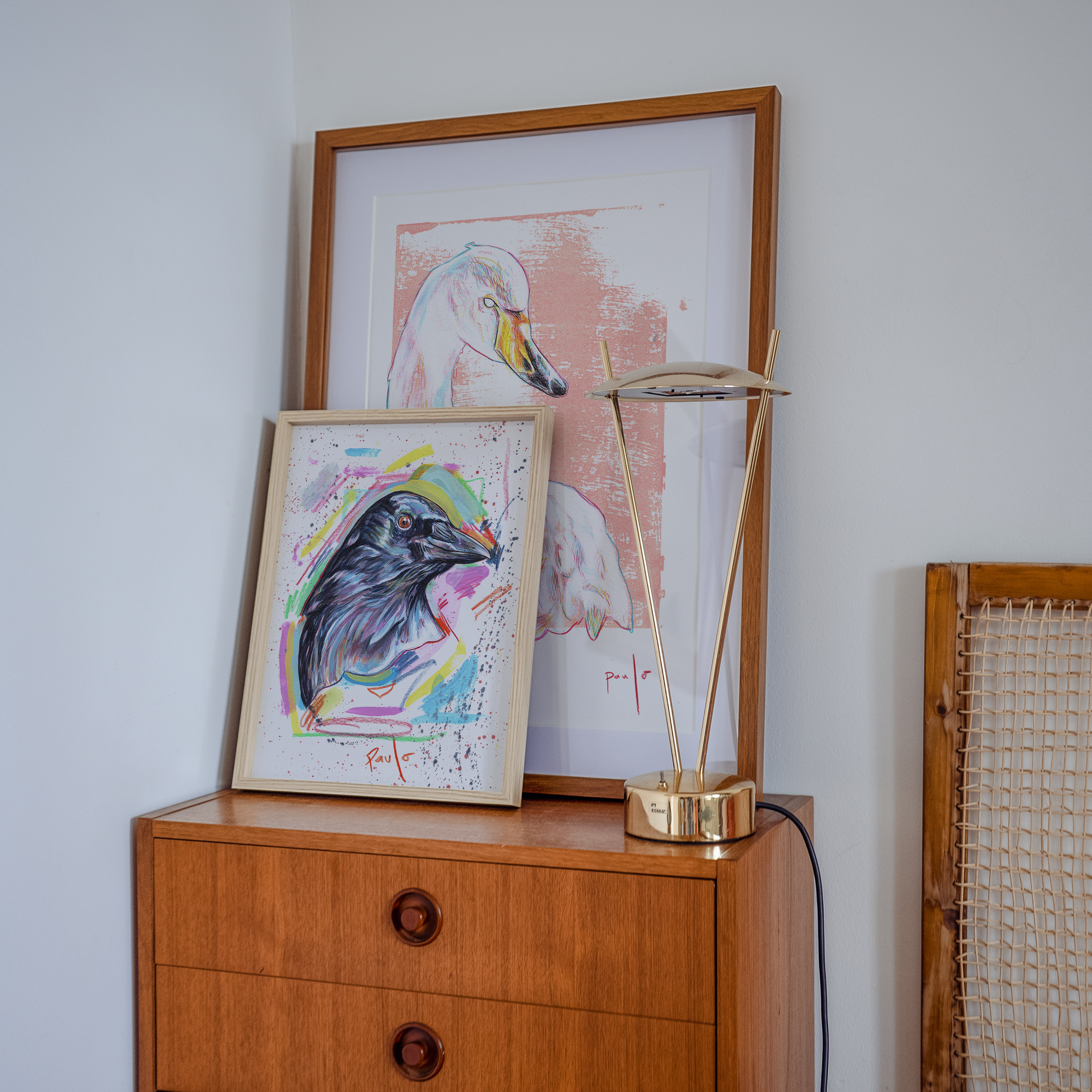 Wooden cabinet with framed artwork and a lamp against a light gray wall