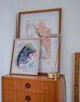 Wooden cabinet with framed artwork and a lamp against a light gray wall