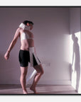 Photo print of a person wearing a white top and black shorts with a neck brace in a room with a light source casting shadows.