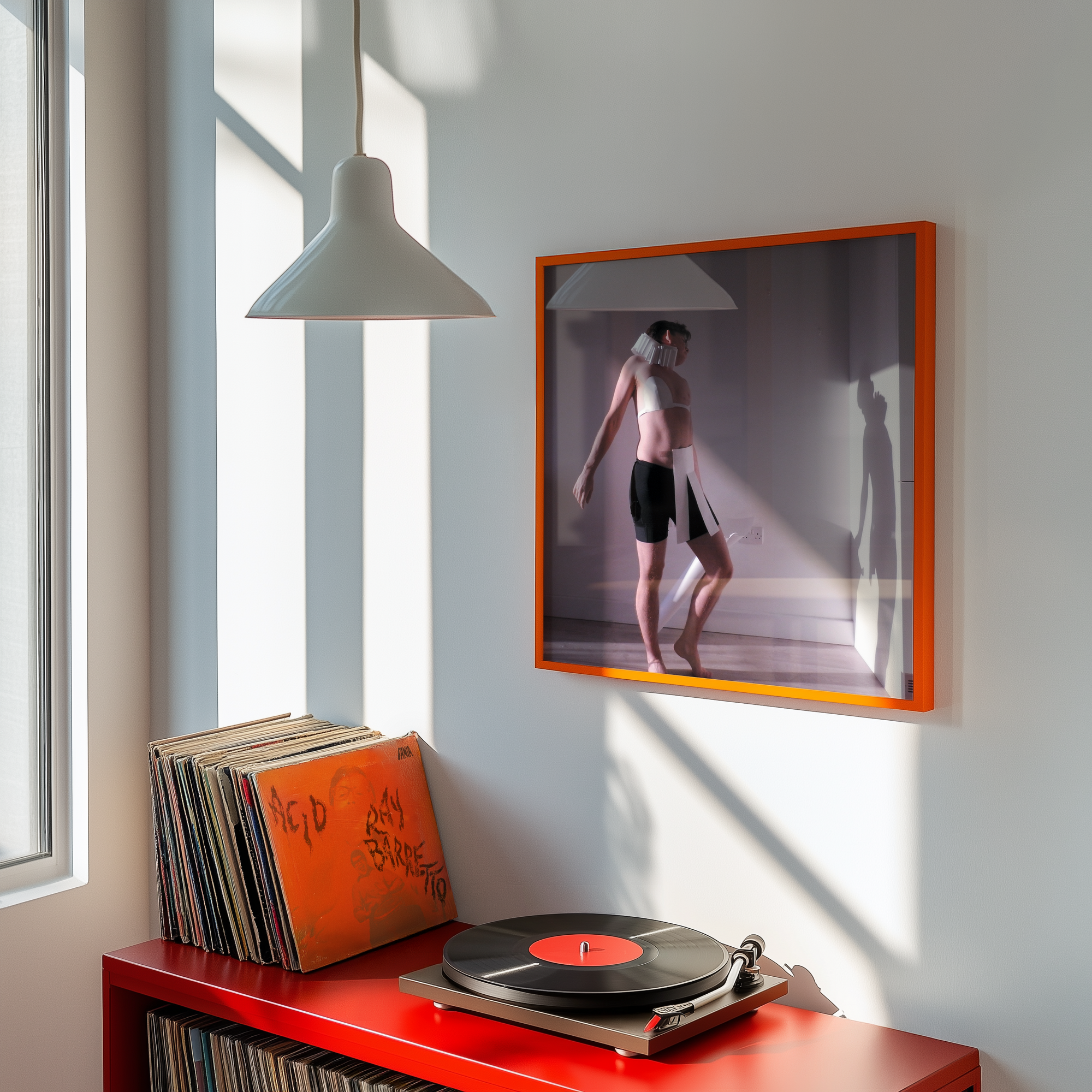 Record player with vinyl records on a red console next to a framed photograph on a white wall.