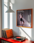 Record player with vinyl records on a red console next to a framed photograph on a white wall.
