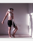Dance art print of a person wearing a white and black outfit with a neck brace in a room with a light source casting a shadow.