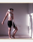 Person wearing a white top and black shorts with a neck brace, standing in a room with a light source casting shadows.