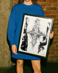 Person holding a framed black and white artwork against a brick wall.