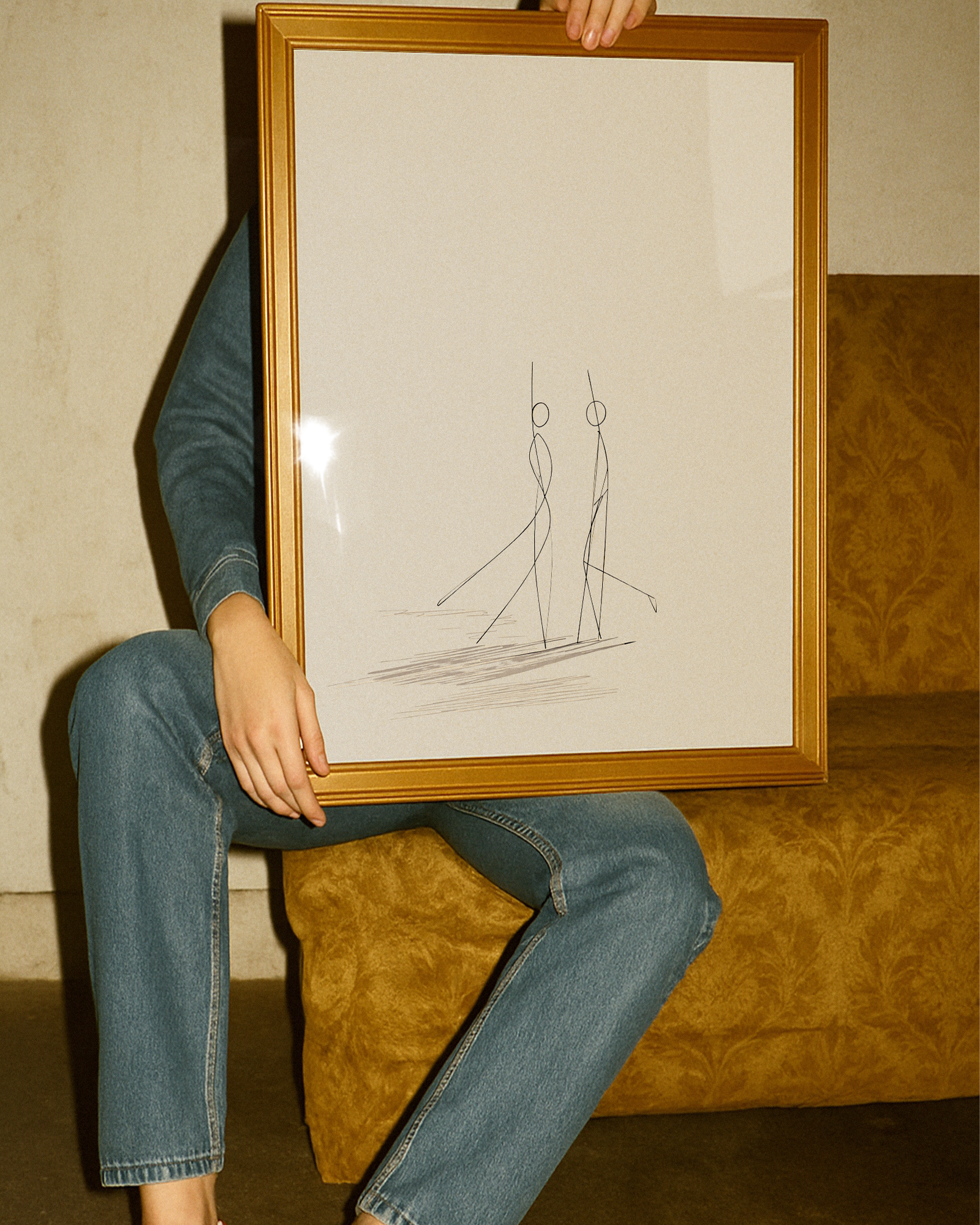 Person holding a framed drawing of two abstract figures against a textured wall.