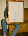Person holding a framed drawing of two abstract figures against a textured wall.