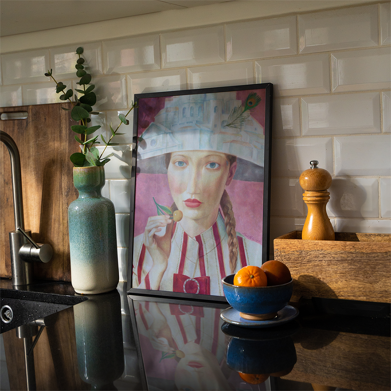 Kitchen counter with a framed portrait, vase, and bowl of fruit against a tiled wall.