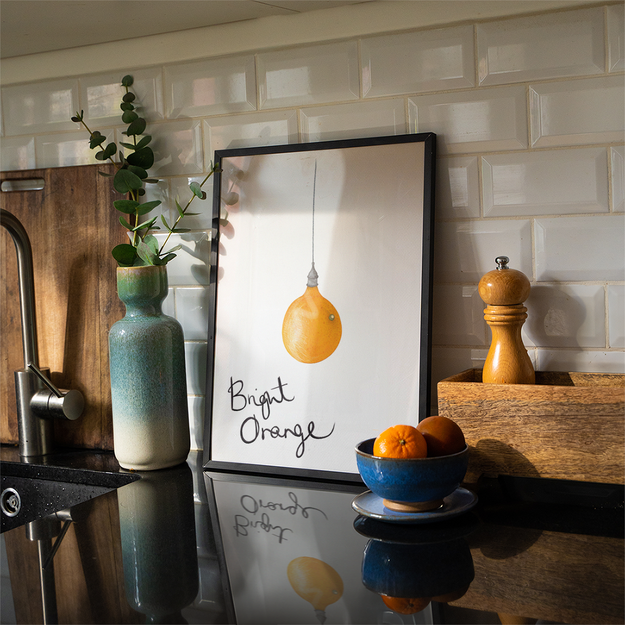 Kitchen counter with a framed print of an orange, a bowl of oranges, and a vase.