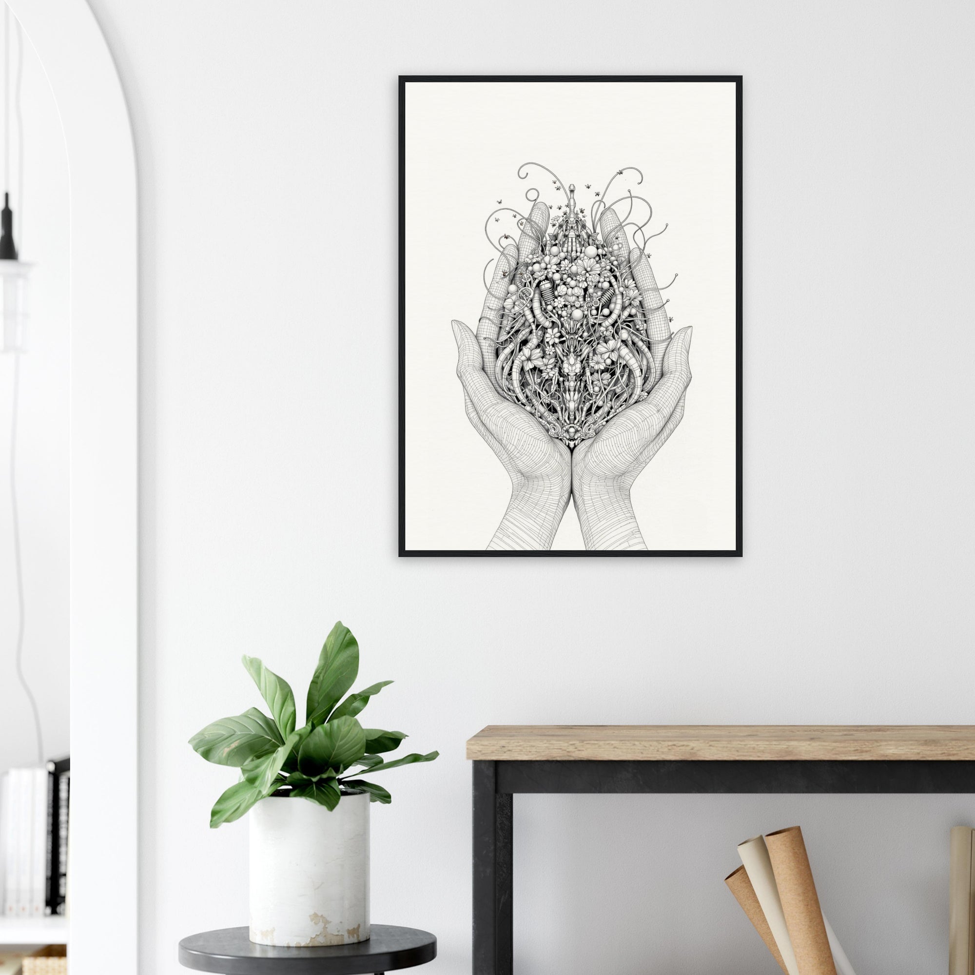 Framed black and white artwork of hands holding a floral design on a wall above a desk with a plant.