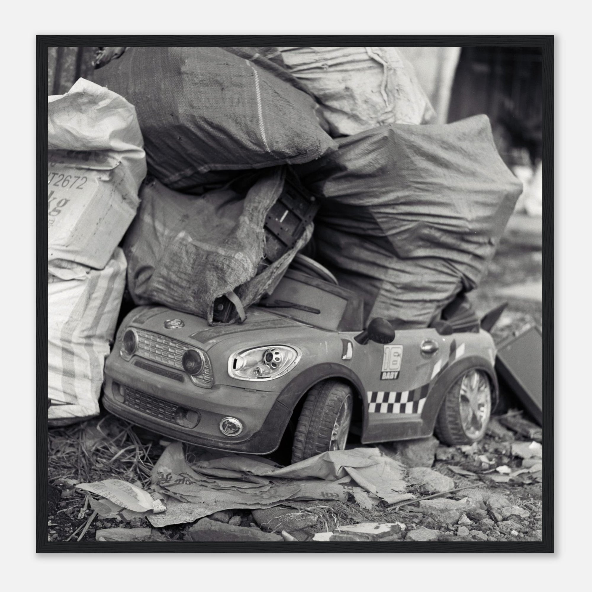 Framed art of a toy car with police design on a pile of newspapers and bags
