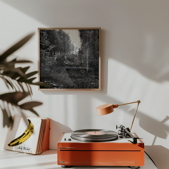 Orange record player on a white surface with a framed black and white artwork on the wall.