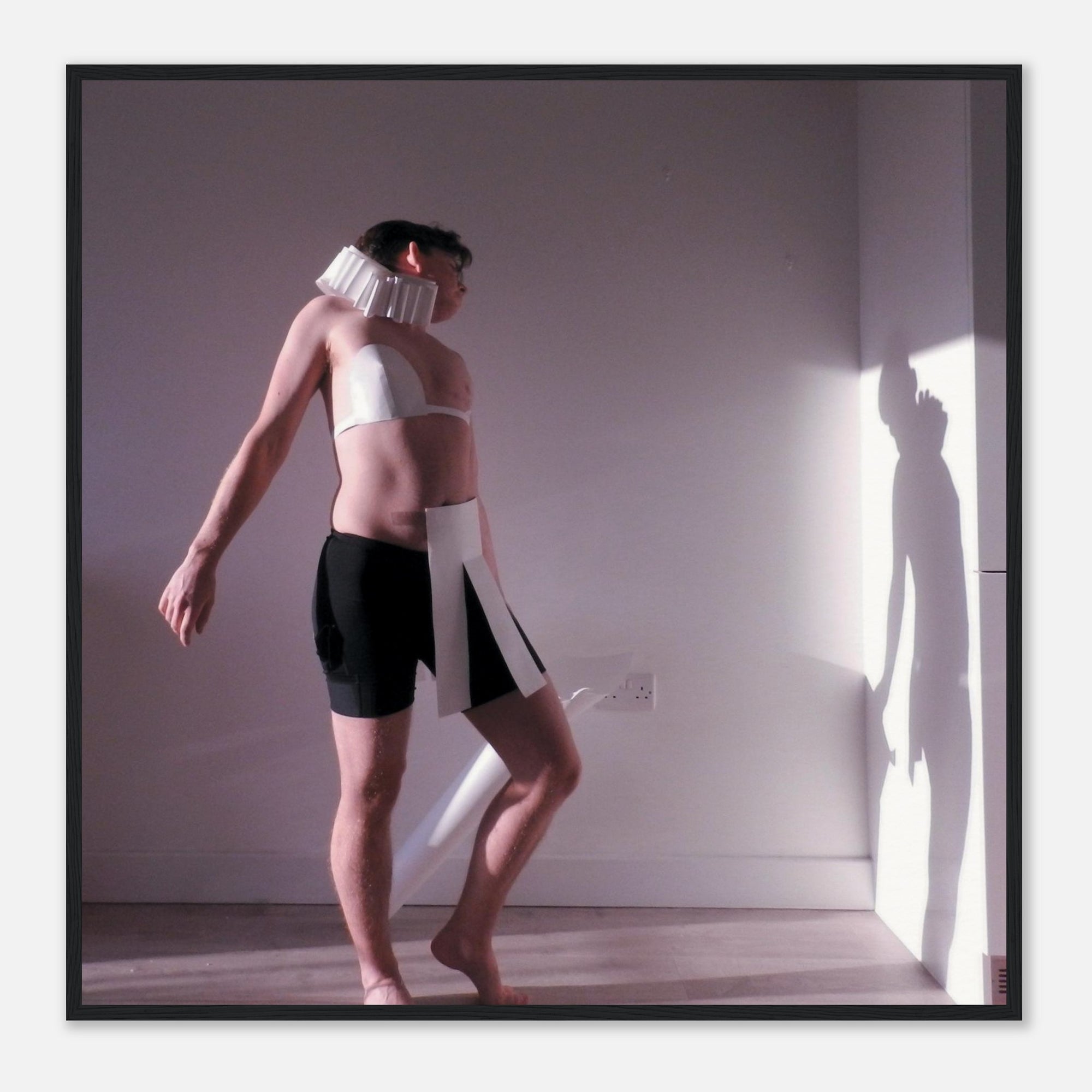 Photo print of a person wearing a white top and black shorts with a neck brace in a room with a light source casting shadows.