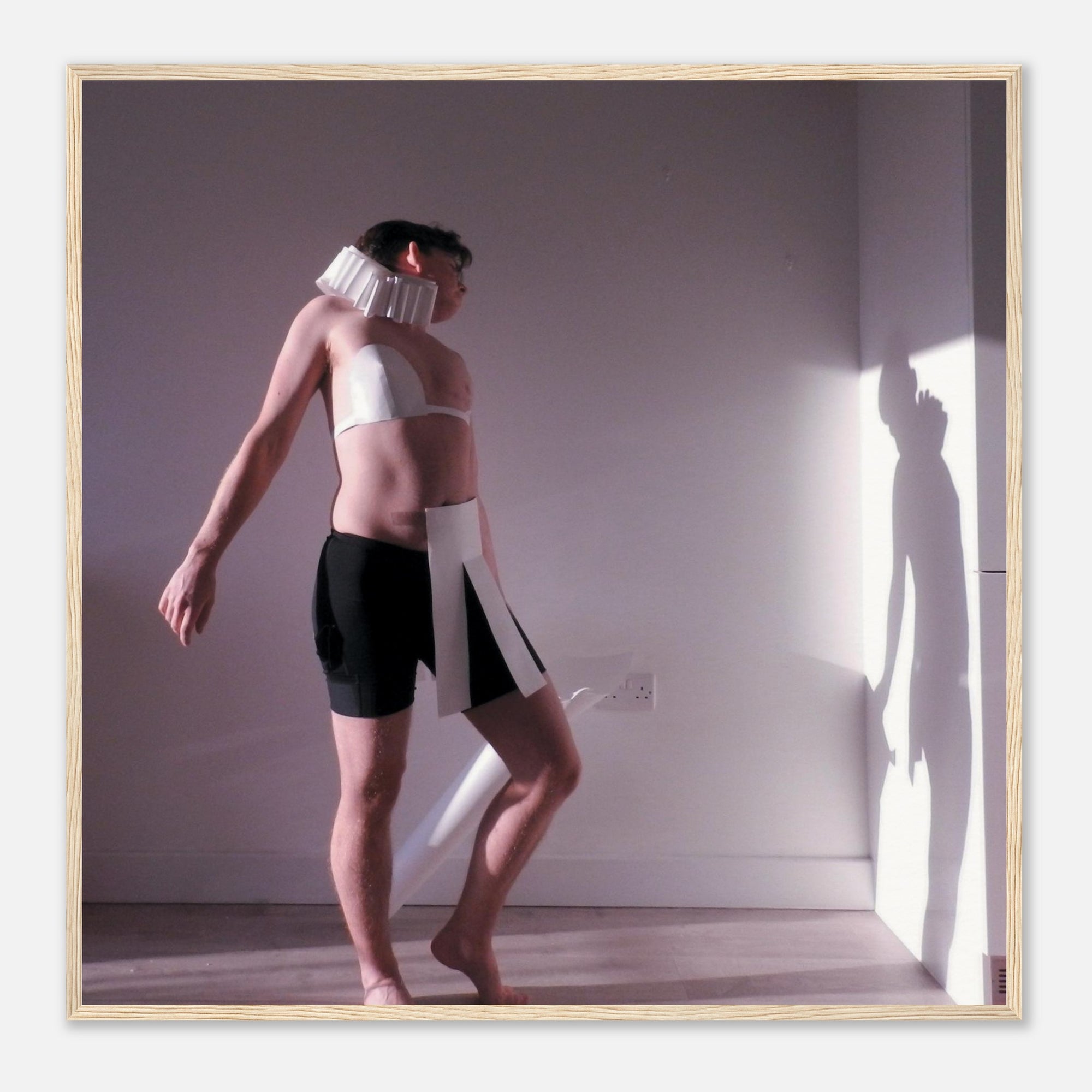 Person wearing a white top and black shorts with a neck brace, standing in a room with a light source casting shadows.