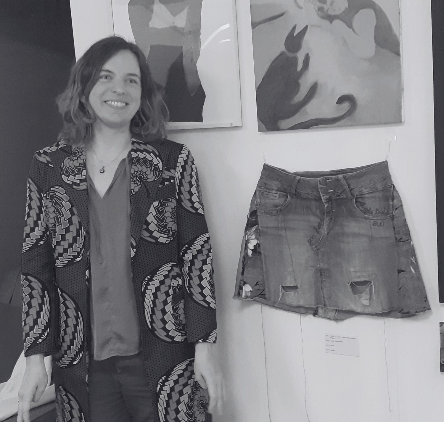 Person standing next to a skirt on a mannequin in an art gallery setting