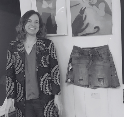 Person standing next to a skirt on a mannequin in an art gallery setting