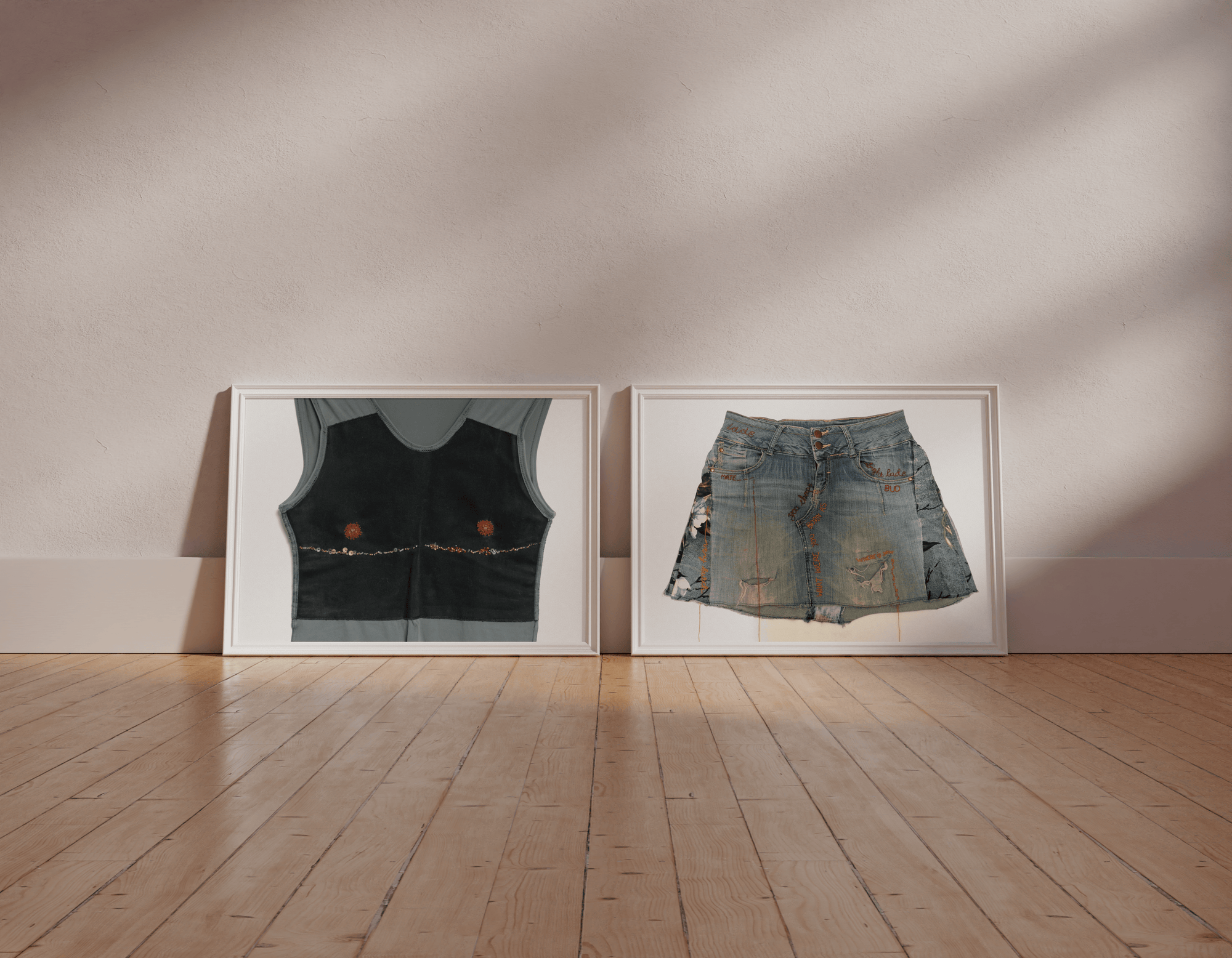 Two framed artworks of a black vest and denim skirt on a wooden floor with a beige wall.