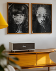 Two framed black and white portraits above a wooden cabinet with a JVC speaker.